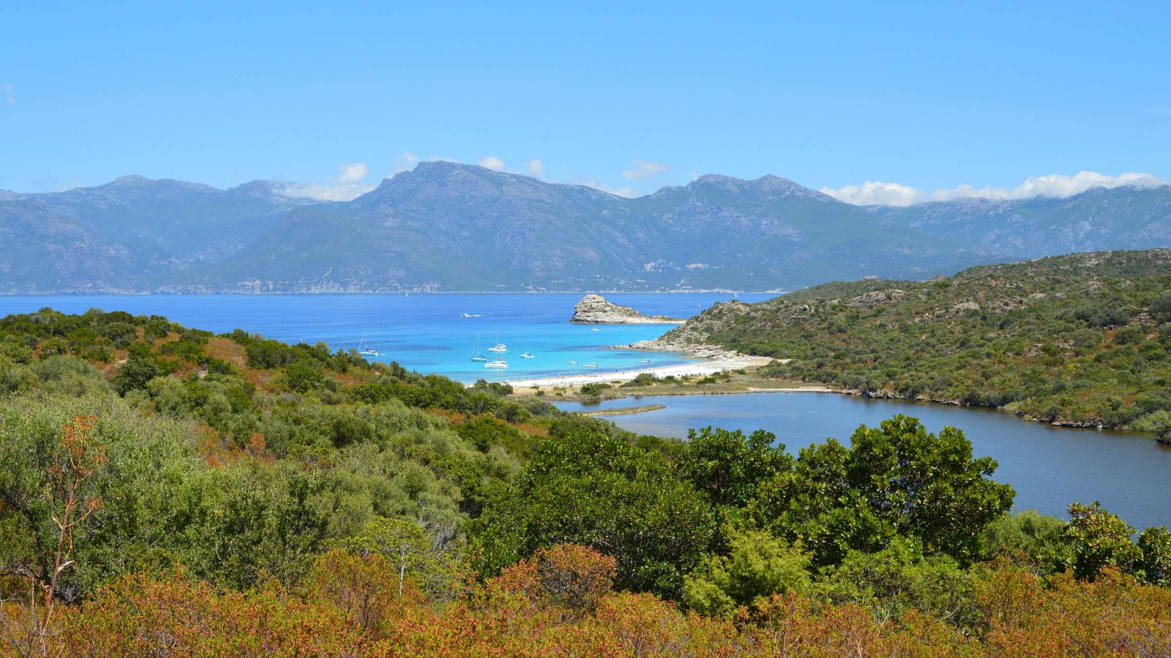 Baie turquoise bordée de maquis, au pied des montagnes corses