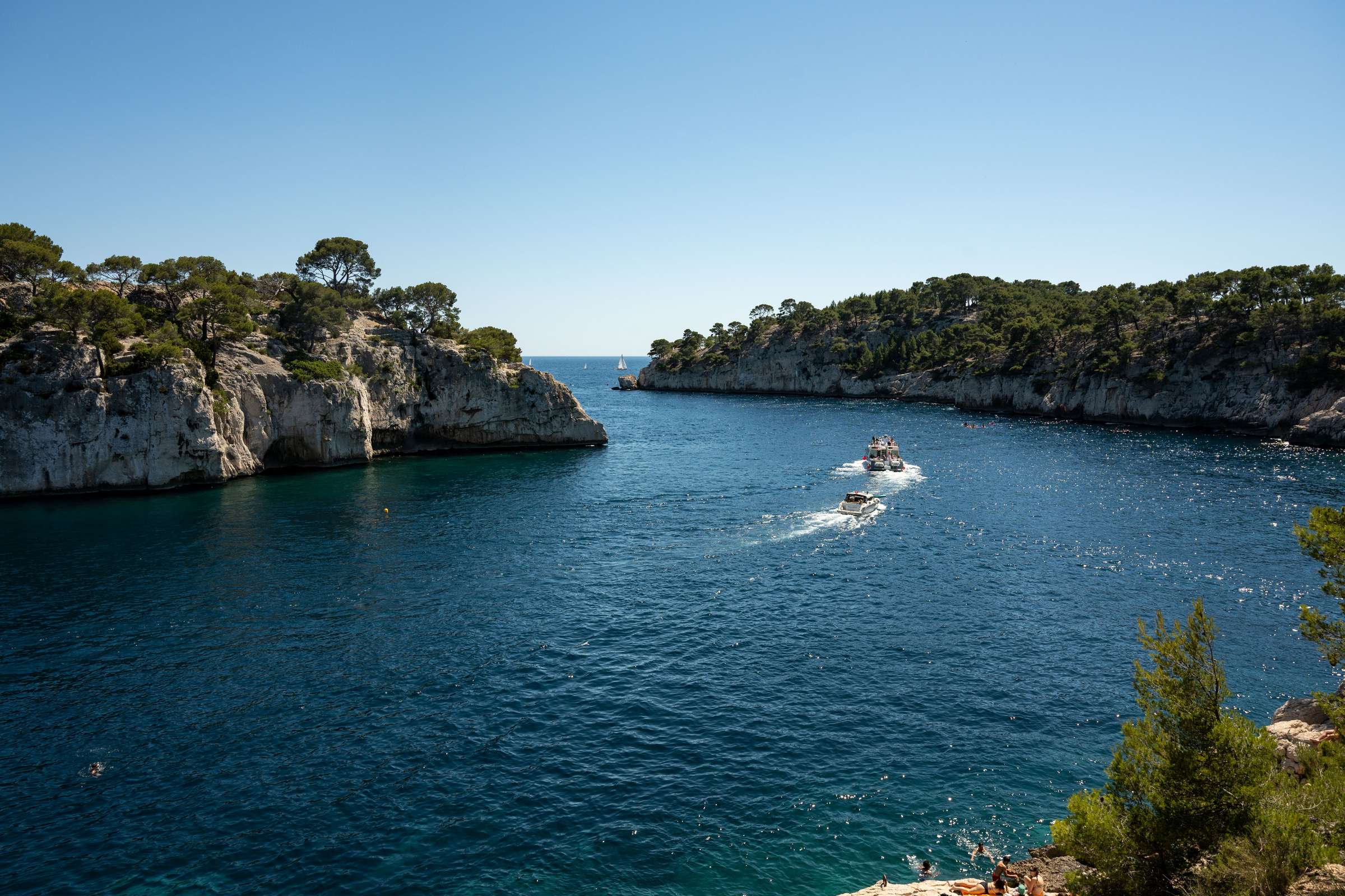 Calanque aux eaux turquoise entre deux falaises calcaires bordées de pins